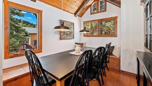Un comedor con mesa de madera, sillas negras y un gran ventanal con vistas al exterior.