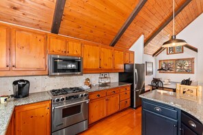A kitchen with wooden cabinets, stainless steel appliances, granite countertops, and a hanging light fixture. - Aspen Escape by Destination Big Bear: Incredible Views and Game Table. Close to Bear Mountain and the Zoo! EV Charger! (Big Bear Lake CA)