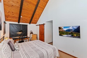 A bedroom with a bed, a desk, a chair, a TV, and a painting of a mountain landscape. - Aspen Escape by Destination Big Bear: Incredible Views and Game Table. Close to Bear Mountain and the Zoo! EV Charger! (Big Bear Lake CA)