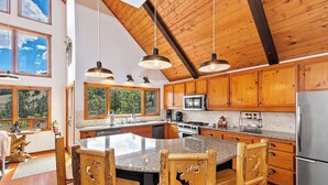 Una cocina amplia con armarios de madera, una isla de granito e iluminación colgante.