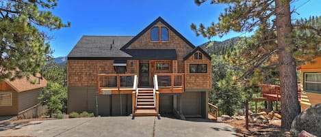 A two-story log cabin with a front porch, a garage, and a mountain backdrop.