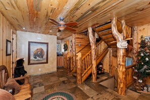 A rustic interior with wooden walls, a staircase, a ceiling fan, and a bear-themed artwork. - Eagle View Lodge by Destination Big Bear: Beautiful Custom-Built Luxury Lakeview Cabin Located in Castle Glen Estates! Spa!Pool Table! Air Conditioning Throughout Home! (Big Bear Lake)