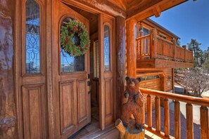 A wooden cabin with a porch, a bear sculpture, and a wreath on the door. - Eagle View Lodge by Destination Big Bear: Beautiful Custom-Built Luxury Lakeview Cabin Located in Castle Glen Estates! Spa!Pool Table! Air Conditioning Throughout Home! (Big Bear Lake)