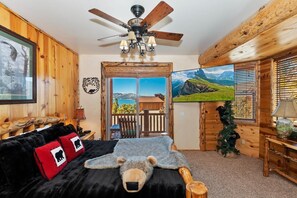 Una habitación acogedora tipo cabaña de madera con cama, ventilador de techo, un cuadro enmarcado y vistas al exterior.