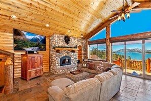 A log cabin interior with a stone fireplace, a large television, and a sofa.