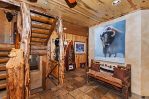 Un interior rústico con una escalera de madera, una escultura de oso, un cuadro enmarcado de toro y un banco.