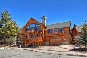 A large, multi-story log cabin with a prominent chimney, multiple balconies, and a garage.