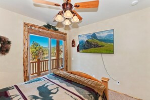 Un dormitorio con cama, ventilador de techo, un cuadro y vistas por una puerta.
