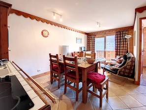A dining area with a wooden table and chairs, a kitchen area with a stove, and a balcony with a view. - Bright apartment near slopes, balcony, 6 people (Les Menuires)