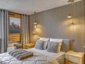 A bedroom with a bed, two bedside tables, a nightstand, a lamp, and a wall-mounted light fixture.