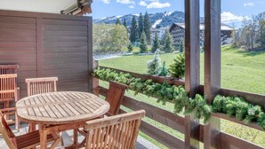 A wooden deck with a round table and chairs, overlooking a green landscape with trees and buildings. - Charming 2-bedroom apartment with fireplace and parking in Megève (Megève)