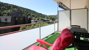 Un balcón con vistas a una ladera boscosa, una mesa y una silla roja.