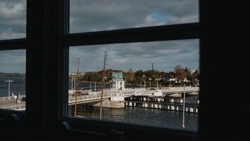 A view of a bridge over water with a small building on the left and houses in the background.