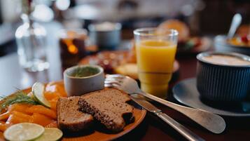 Frühstückstisch mit Lachs, Brot, einem Glas Orangensaft und einer kleinen Portion grünem Aufstrich auf einem Teller.
