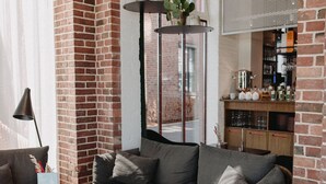 A cozy living area with a sectional sofa, a round table, and a green armchair. A hanging plant and a brick wall add character to the space. - Südspeicher (Kappeln)