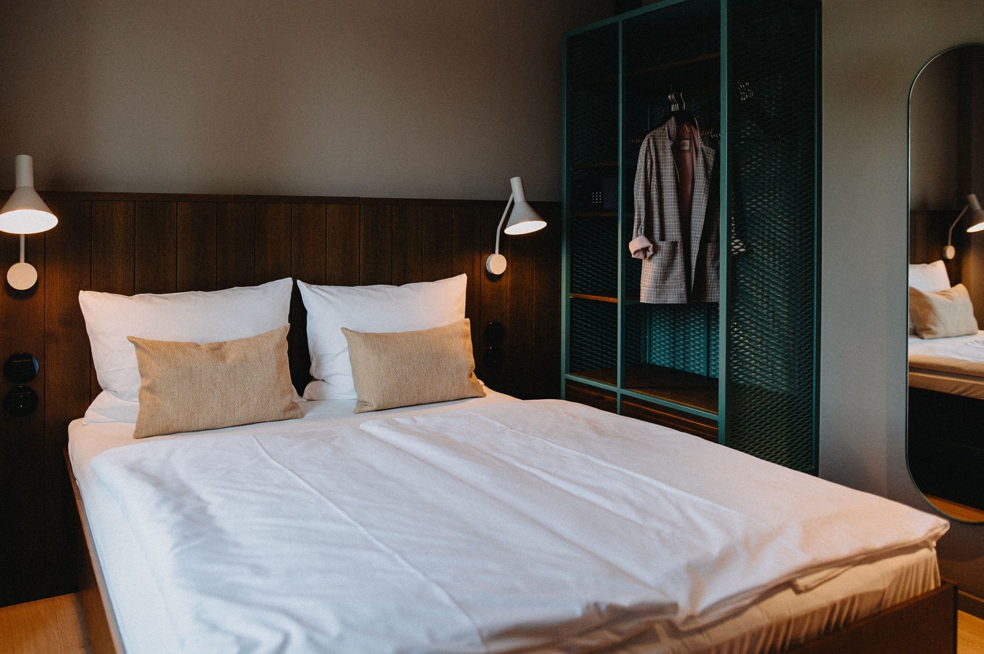 Een keurig opgemaakt bed met witte lakens en twee beige kussens, met aan weerszijden wandlampen.