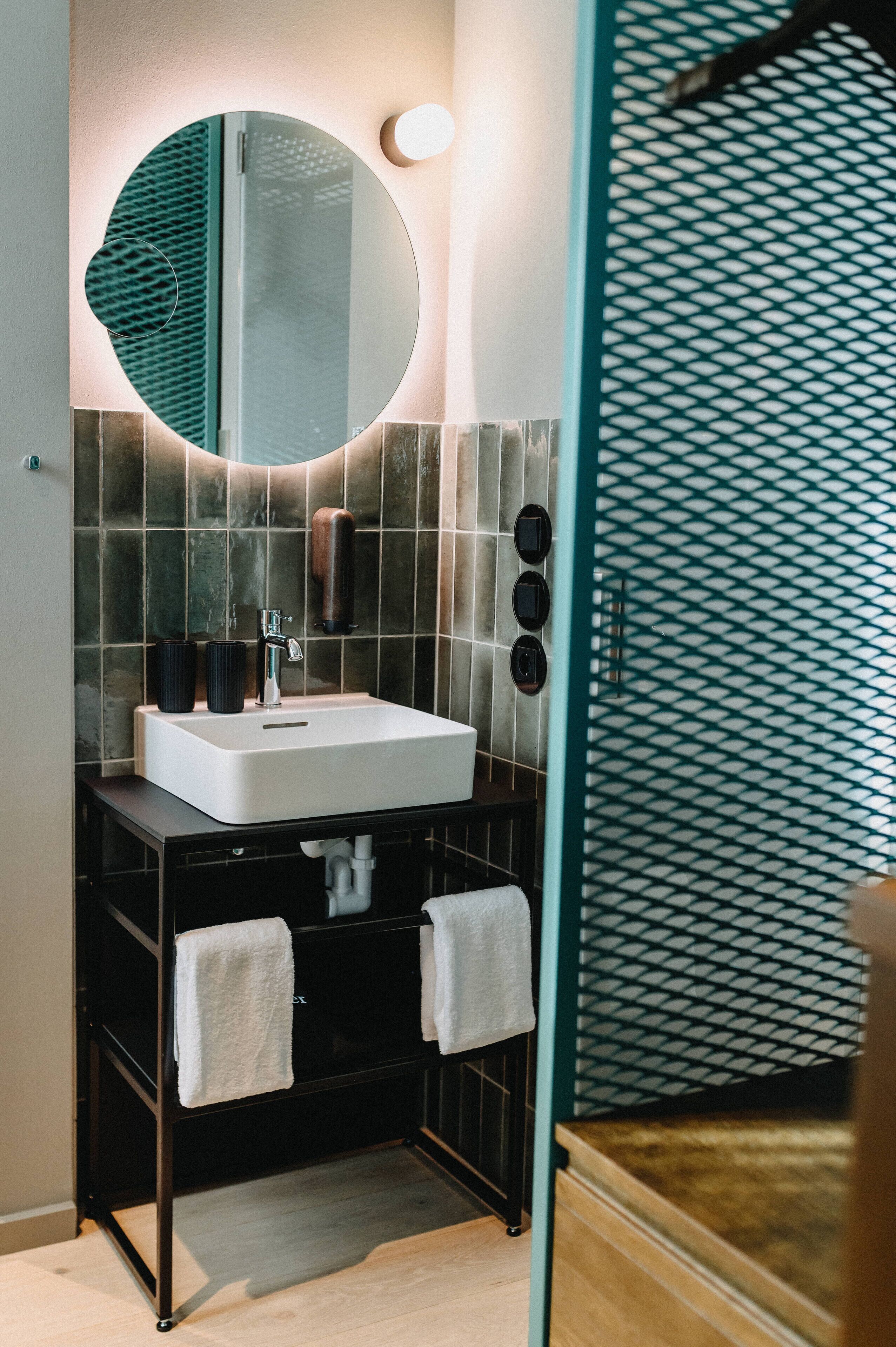 A modern bathroom with a round mirror, a white sink, and a towel rack.
