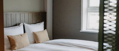 A neatly made bed with a wooden headboard, a hanging light fixture, and a window with blinds.