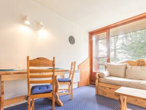 A cozy room with a wooden dining table, two chairs, a sofa, and a window with a view of trees.