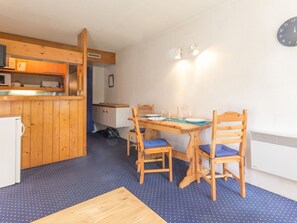 Una cucina compatta con mobili in legno, un forno a microonde e un lavello. C'è un'area pranzo con un tavolo e sedie in legno, e una sveglia appesa al muro.