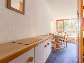 Una cucina compatta con mobili in legno e un piano di lavoro, una zona pranzo con tavolo e sedie, e un'ampia finestra che offre luce naturale.
