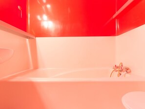 A modern bathroom with a white bathtub, a white toilet, and a red accent wall. - Ski-in/Ski-out Studio with Balcony (Les Arcs 1800)