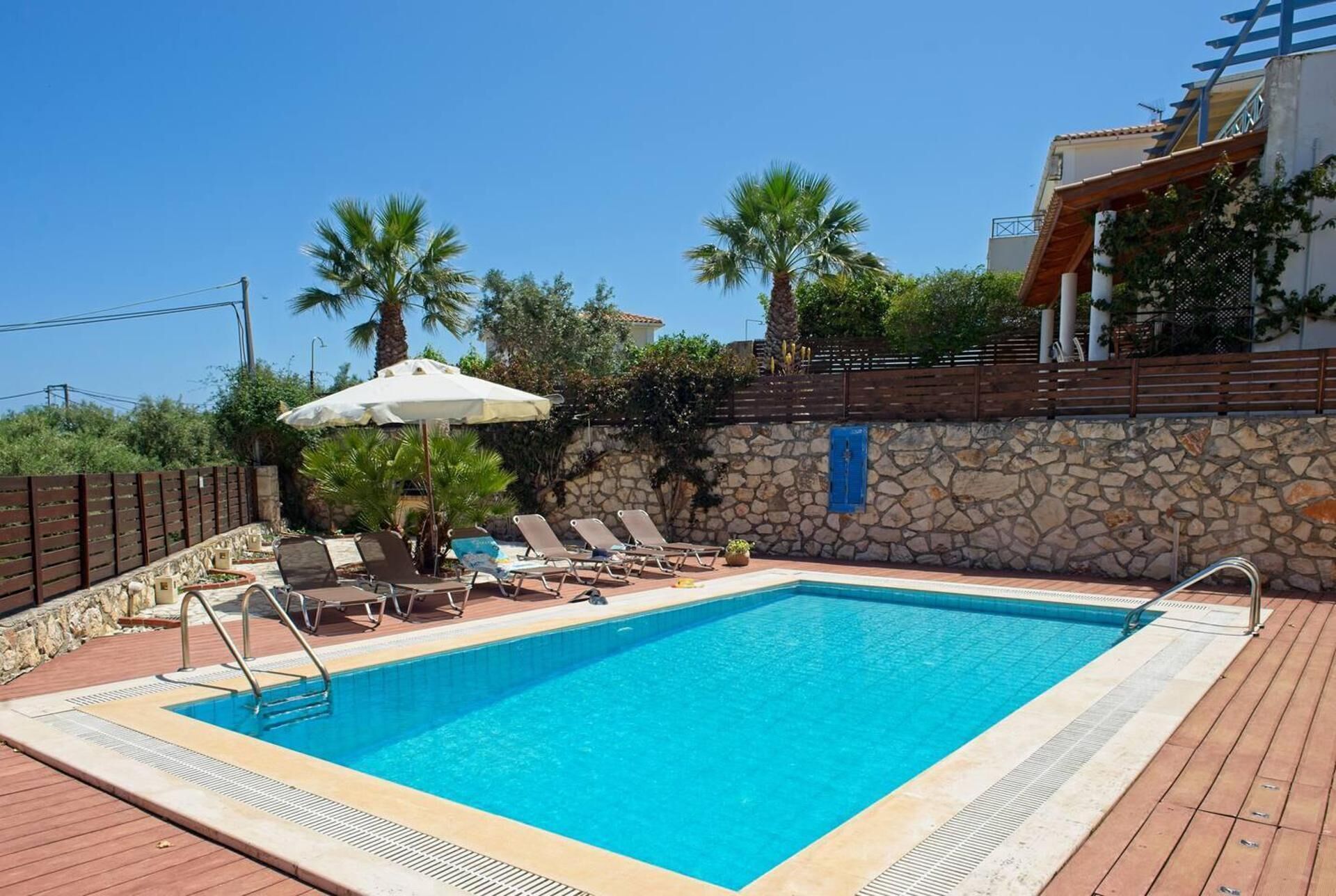 A rectangular swimming pool with a stone wall and a wooden deck surrounding it.