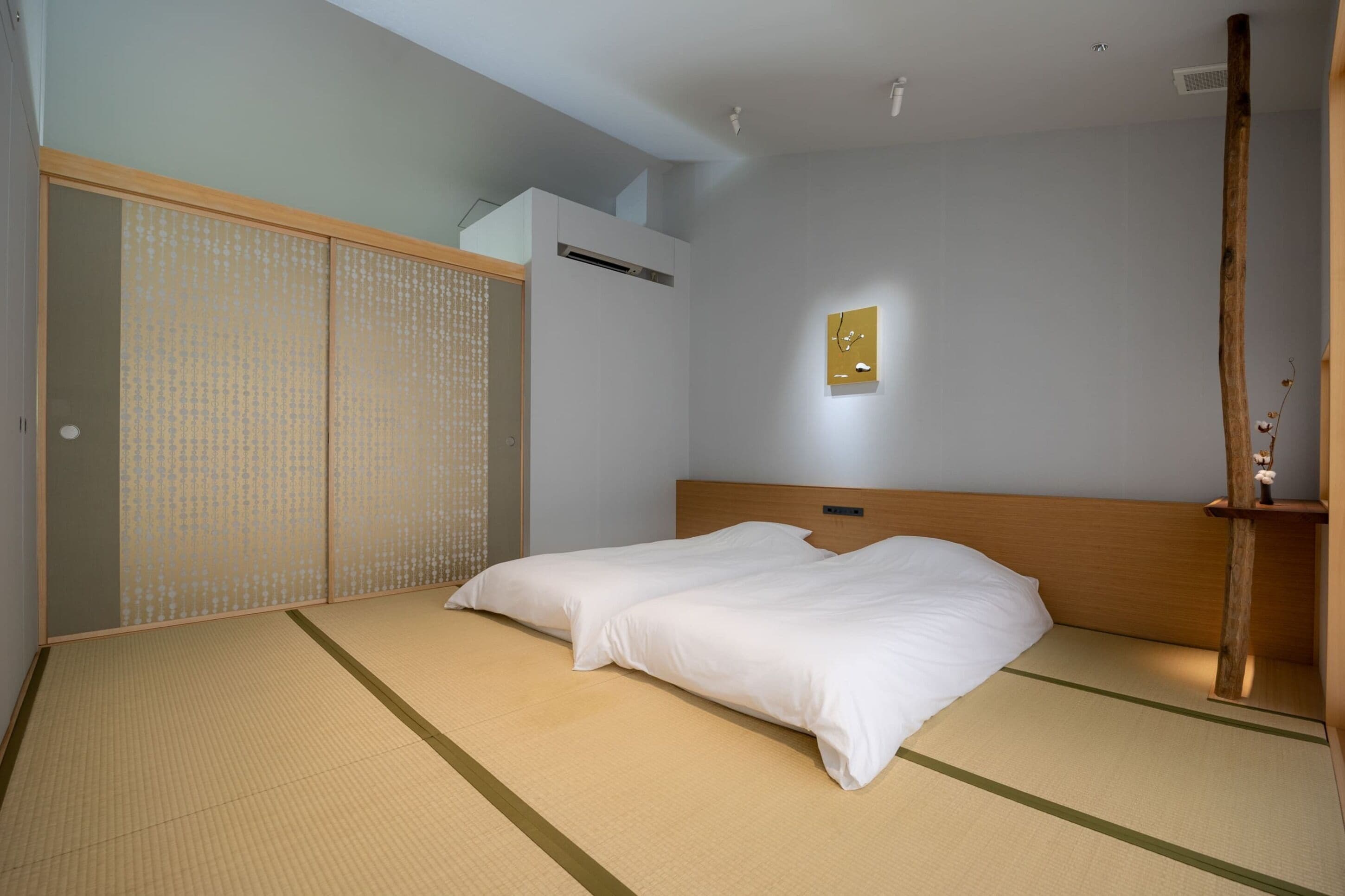 A traditional Japanese-style room with tatami flooring, a low wooden bed, and a shoji screen door.