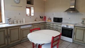 A kitchen with a white table, red chairs, a stove, a microwave, and a sink. - Charming Detached Cottage with Large Garden, Near Forest and Karting (La Celette)