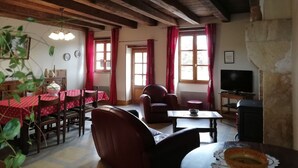 A cozy room with a wooden ceiling, a dining table with chairs, a sofa, a television, and a fireplace. - Charming Detached Cottage with Large Garden, Near Forest and Karting (La Celette)