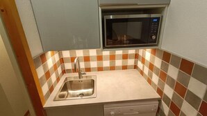 A compact kitchen with a stainless steel sink, a microwave, and a dishwasher. The backsplash features a checkered tile pattern.