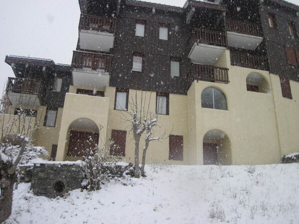 A multi-story building with balconies and arched doorways, surrounded by snow.
