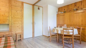 A room with a wooden floor, a dining table set with chairs, a small bench, and a door.
