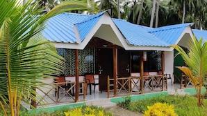 A bungalow with a blue roof, wooden deck, and outdoor seating area surrounded by greenery. - Honey Moon Beach Resort (Port Blair)