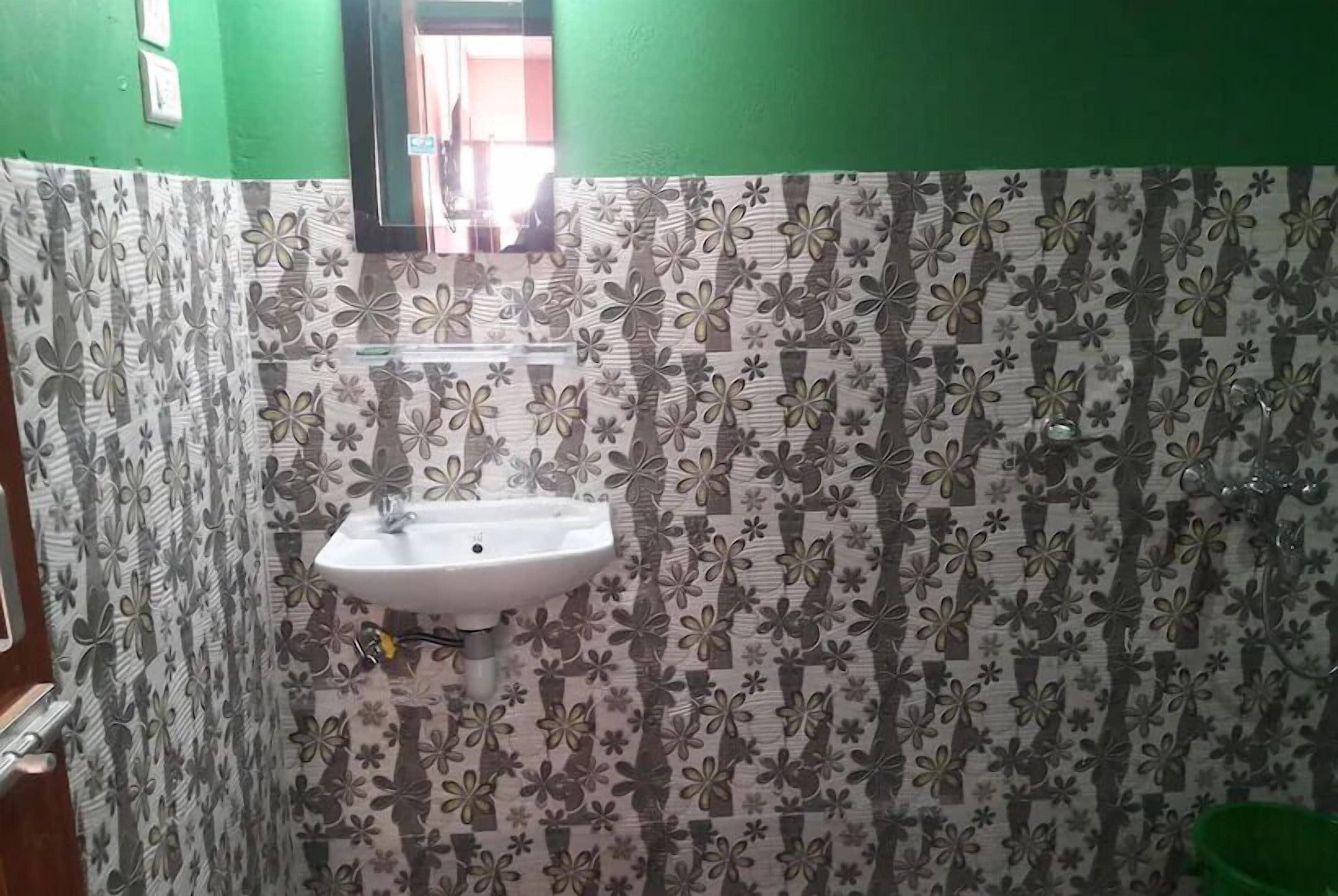 Un baño con lavamanos blanco, paredes verdes y papel tapiz estampado.
