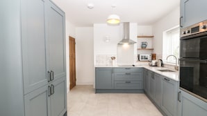 A modern kitchen with grey cabinets, a stainless steel range hood, a microwave, and a double oven. - Angorfa (Pwllheli)