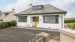 A two-story house with a yellow front door, white exterior walls, and a grey roof. - Angorfa (Pwllheli)