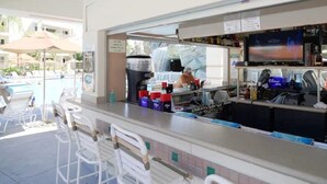 A bar area with a pool view, bar stools, and a television screen.