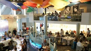 A spacious, multi-level dining area with a modern design, featuring a central glass railing and a variety of seating arrangements.
