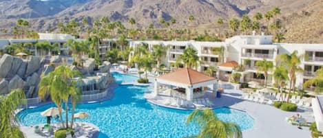 Un resort con una amplia piscina, palmeras y montañas al fondo.