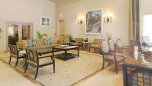 A spacious living area with a sofa, chairs, a coffee table, and a dining table. There are wall-mounted lights and artwork.
