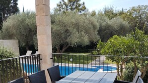 Une terrasse extérieure avec une table et des chaises, une piscine et de la verdure tout autour.