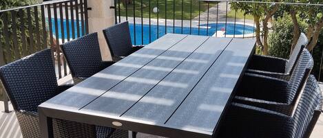 An outdoor patio with a table and chairs, a pool, and surrounding greenery.