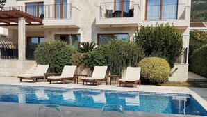 Un bâtiment moderne à deux étages, doté d’une piscine, de chaises longues et d’une table en bois sur laquelle reposent deux verres de vin rouge.
