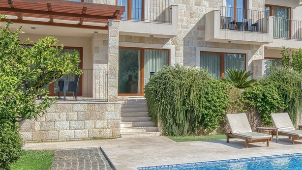 Une maison à deux étages avec une piscine, une façade en pierre et un balcon.