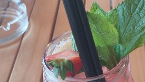 Une carafe en verre avec une paille noire et des feuilles de menthe, contenant une boisson rose.