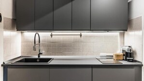 A modern kitchen with grey cabinets, a stainless steel sink, and a coffee machine. - Modern and Spacious Apartment in Noto, Sicily (Noto)