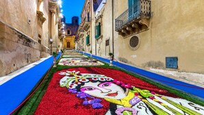 A narrow street with a floral carpet leading to a building with a balcony. - Modern and Spacious Apartment in Noto, Sicily (Noto)