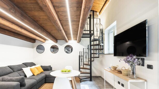 A modern living room with a grey sofa, a round white table, and a spiral staircase. - Modern and Spacious Apartment in Noto, Sicily (Noto)