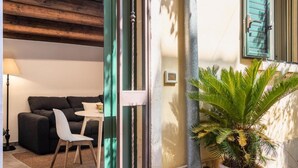 A cozy living area with a sofa, a small table, and a chair. There is a potted plant and a lamp. - Modern and Spacious Apartment in Noto, Sicily (Noto)